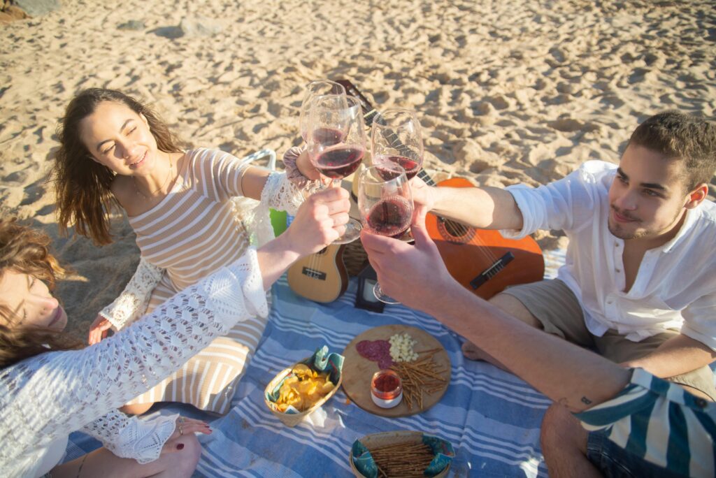 group of young people at the beach having a picnic and cheersing with wine glasses