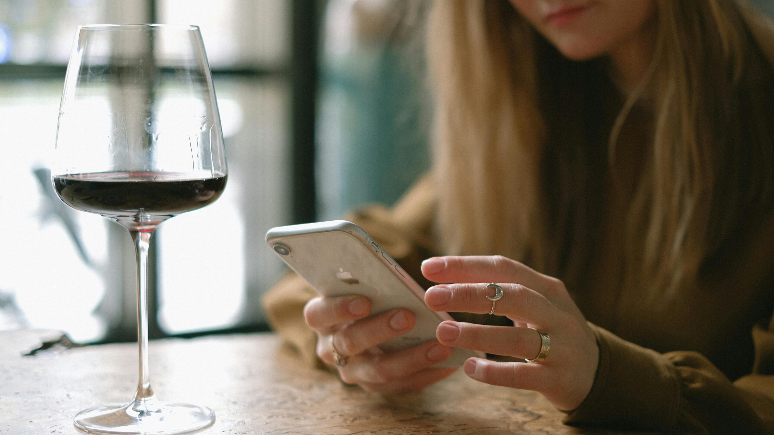 woman scrolling on phone and drinking red wine