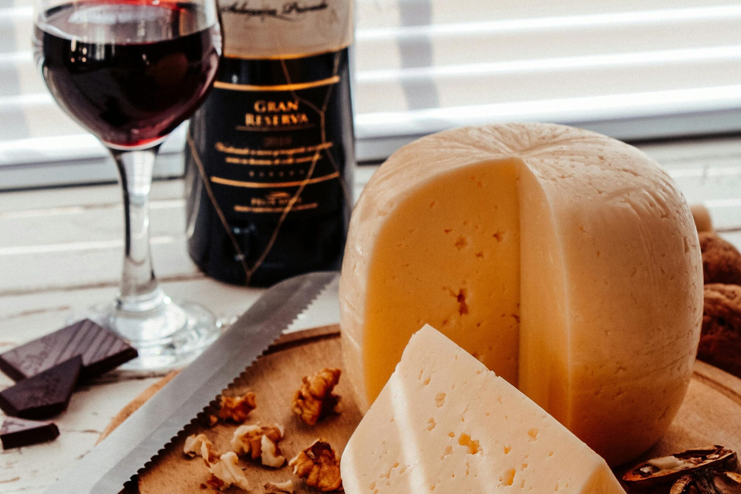 glass of red wine next to block of cheese, chocolate, and walnuts. 