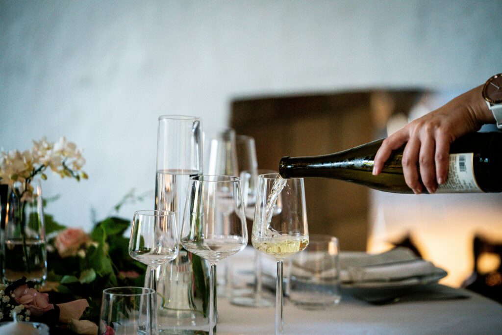 person pouring white wine into glasses on a table