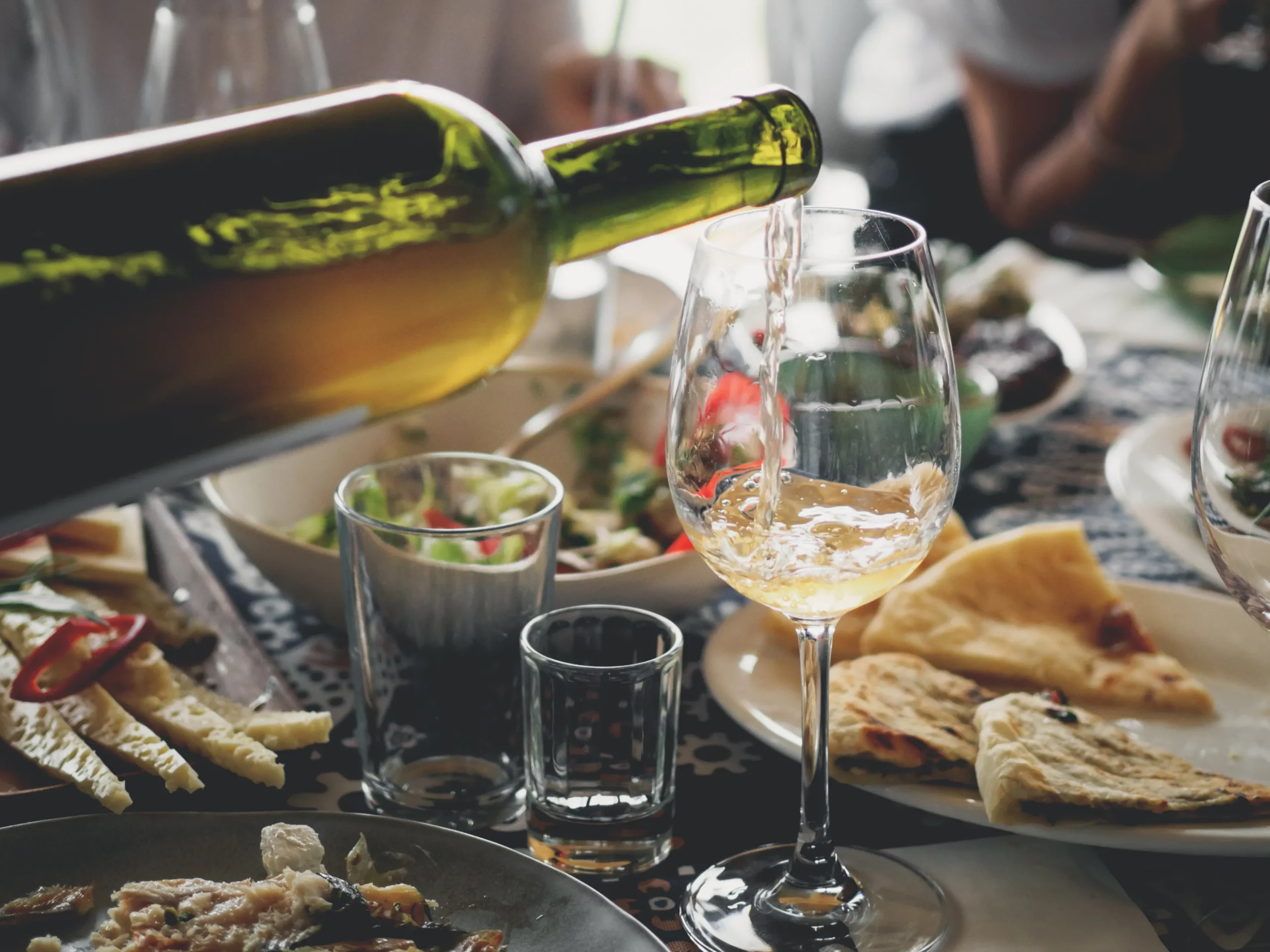 a glass of white wine being poured amidst delicious looking food