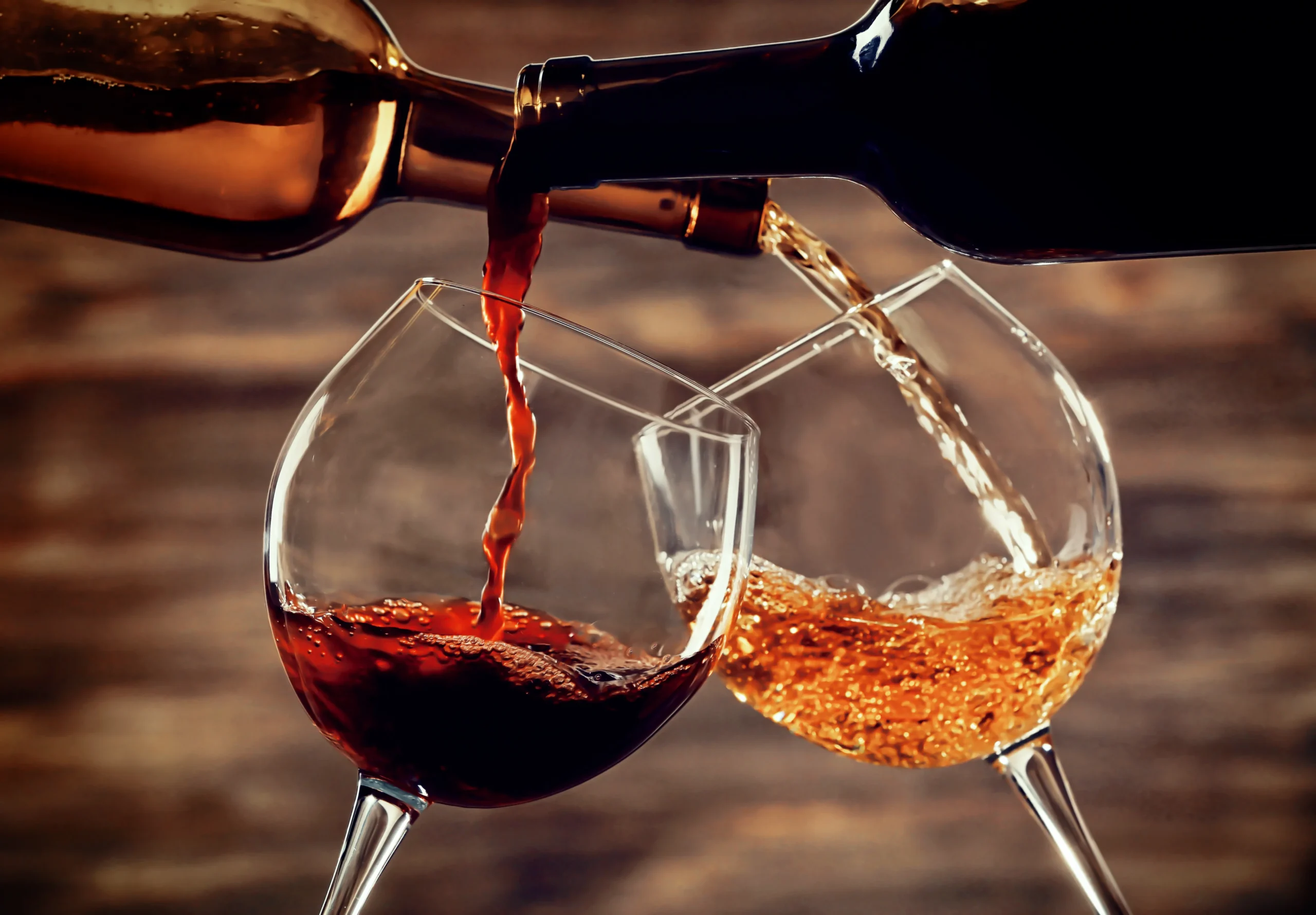 White and red wine pouring in glasses on wooden background