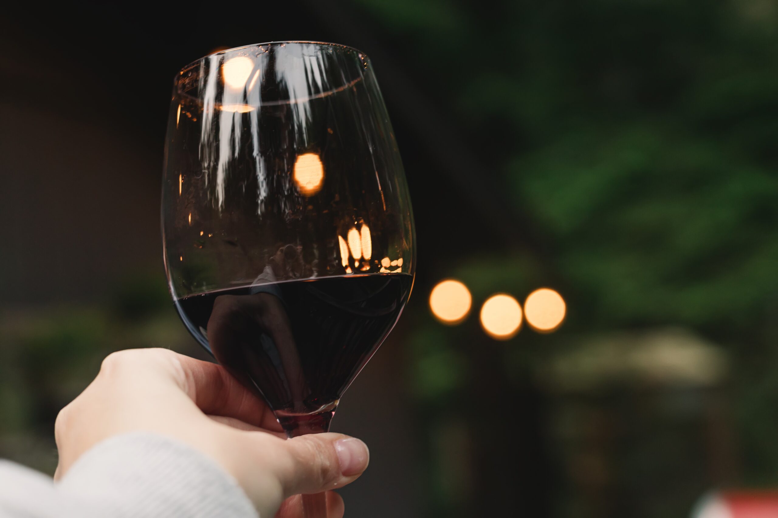 A woman holding a glass of red wine on a serene backyard patio.