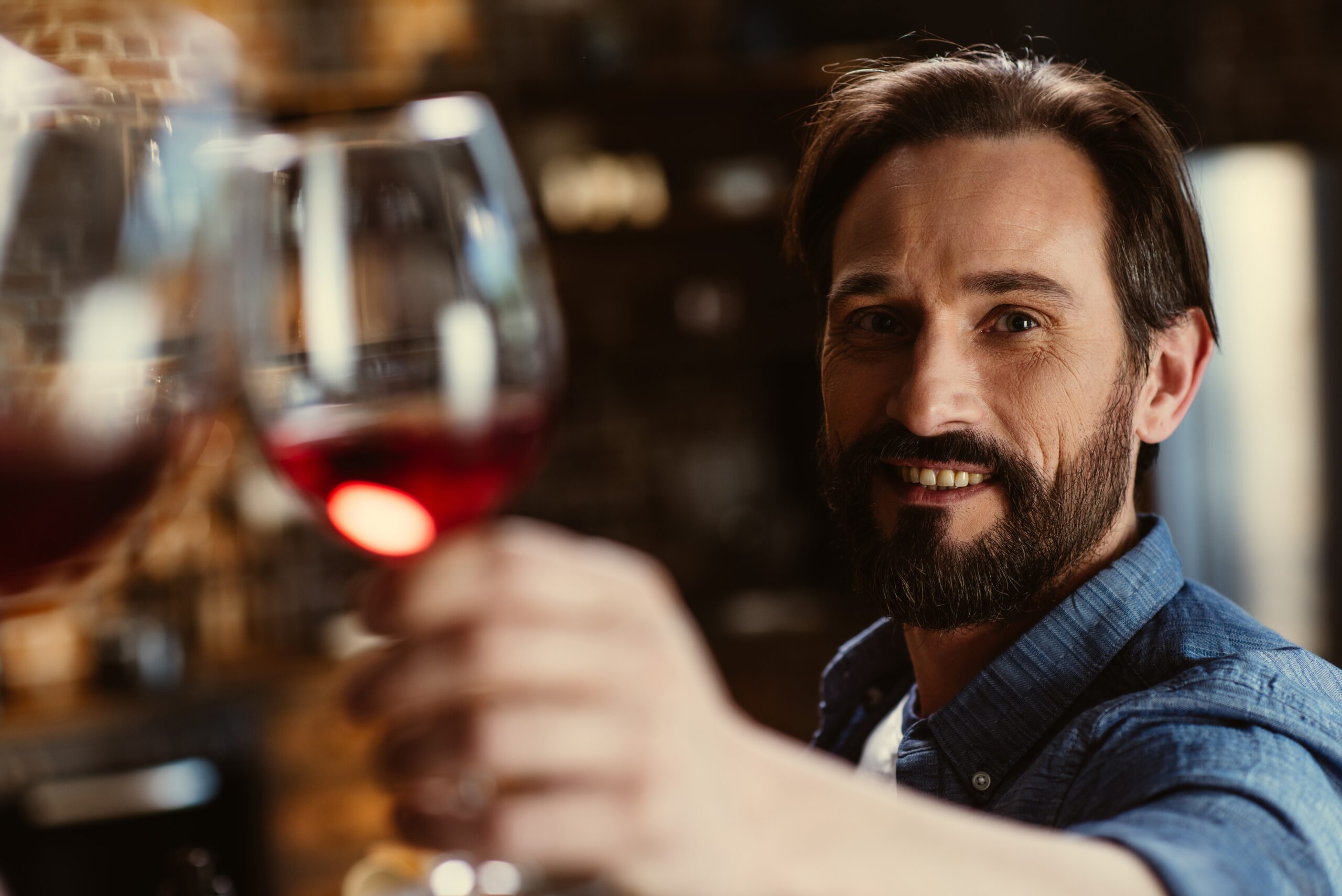 A man toasting with a glass of red wine, cheerful and friendly.